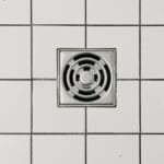 Top view of white ceramic tile floor with stainless steel square shaped cover of drain in contemporary shower